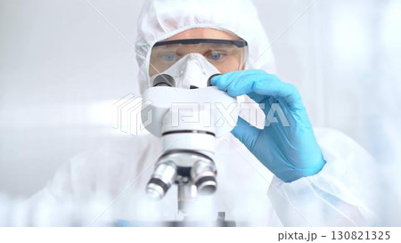 Scientist is analyzing samples using a microscope in a laboratory setting. Close-up of a focused researcher in a protective gear. Science concept Scientist is analyzing samples using a microscope in a laboratory setting. Close-up of a focused researcher in a protective gear. Science concept 130821325