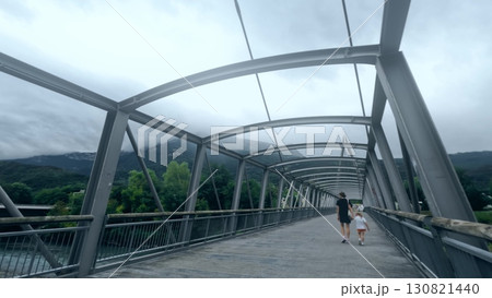 Pedestrian bridge over the Drac river between Echirolles and Seyssins, France, with people walking, mountains in background, and modern steel structure design 130821440