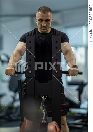 athletic man focuses on his form while doing squats in a gym. He uses squat equipment designed for strength training showcasing determination and effort. 130821660