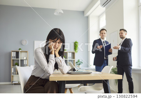 Lonely employee sits at desk as coworkers gossip and exclude her nearby today Lonely employee sits at desk as coworkers gossip and exclude her nearby today 130822594