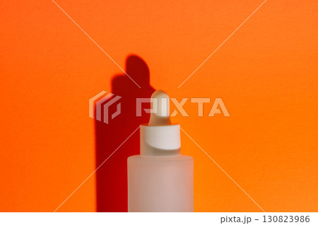 Frosted glass serum bottle with white dropper on orange background and hard shadow 130823986