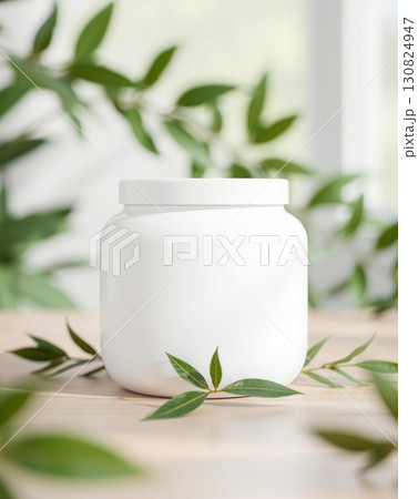 A minimalist white jar with lid is displayed among green leaves on a wooden surface A minimalist white jar with lid is displayed among green leaves on a wooden surface 130824947