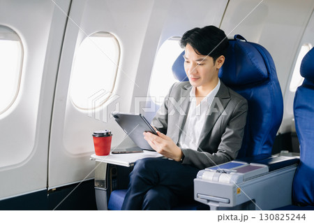 Young Asian executive excels in first class, multitasking with digital tablet, laptop and smartphone. 130825244