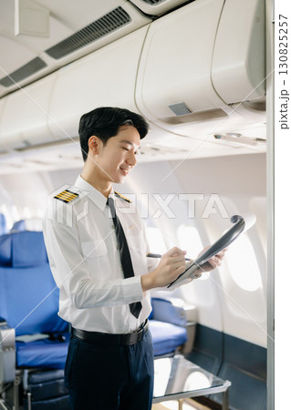 Asian Confident male pilot in uniform leaning at the passenger seat while standing inside of the airplane flight cockpit during takeoff and checking Asian Confident male pilot in uniform leaning at the passenger seat while standing inside of the airplane flight cockpit during takeoff and checking 130825257