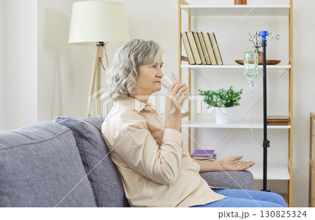 Senior woman sitting on couch, receiving IV drip infusion and vitamin therapy at home or in clinic. Senior woman sitting on couch, receiving IV drip infusion and vitamin therapy at home or in clinic. 130825324