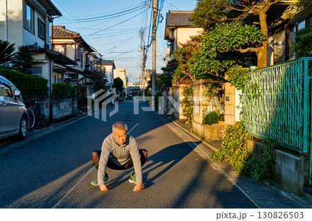 住宅街の道路でストレッチをする高齢男性 130826503