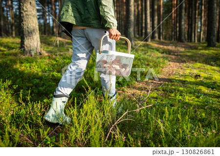 Woman walking through forest on trail carrying basket of mushrooms, fall nature hobby, harvest time Woman walking through forest on trail carrying basket of mushrooms, fall nature hobby, harvest time 130826861