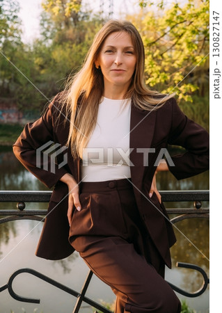 Female confidence. Outdoor portrait. Independent smiling business woman wearing suit posing in spring park at river bank. 130827147