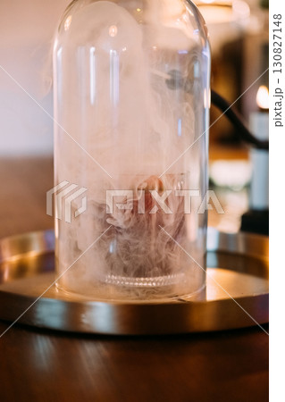 Preparing alcoholic beverage. Pub glassware. Cocktail covered with transparent dome on bar counter. Smoking gun device for flavor. Preparing alcoholic beverage. Pub glassware. Cocktail covered with transparent dome on bar counter. Smoking gun device for flavor. 130827148