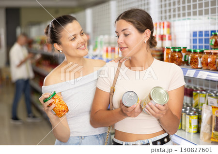 Two female shoppers choosing canned food in grocery store Two female shoppers choosing canned food in grocery store 130827601