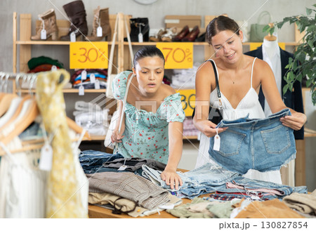 Two young women carefully choosing fashionable jeans or shorts in clothing store Two young women carefully choosing fashionable jeans or shorts in clothing store 130827854