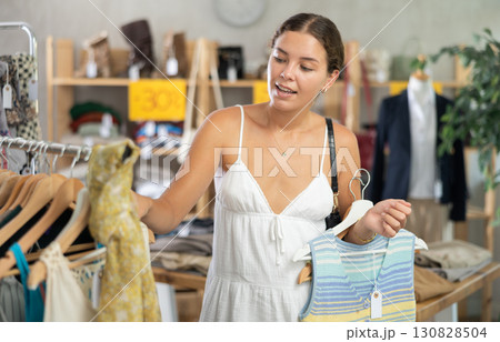 Positive young woman choosing something for summer in clothing store Positive young woman choosing something for summer in clothing store 130828504