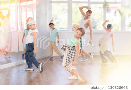 Happy young girl and boy in casual clothes performing hip hop dance in dancing room during training with male teacher Happy young girl and boy in casual clothes performing hip hop dance in dancing room during training with male teacher 130828668