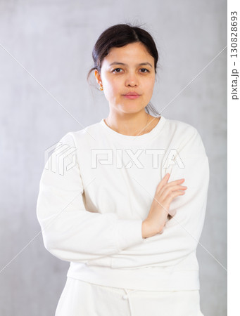Confident young brunette standing with arms crossed on gray background Confident young brunette standing with arms crossed on gray background 130828693