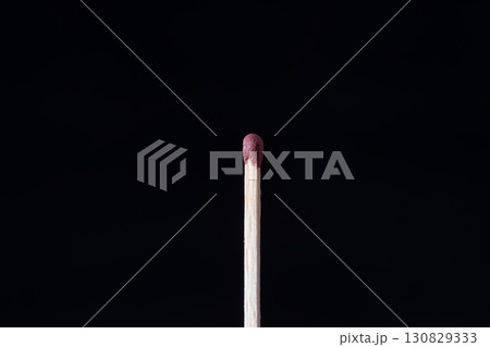 a single matchstick standing upright against a completely dark, black background 130829333