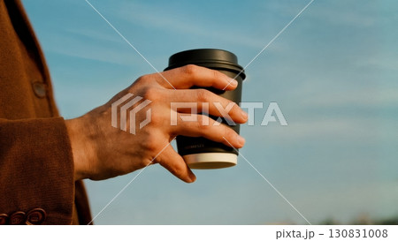 A close-up of a person's hand holding a cup of coffee. Coffee break, a moment of reflection, business pause A close-up of a person's hand holding a cup of coffee. Coffee break, a moment of reflection, business pause 130831008