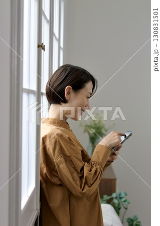 窓辺でスマホを操作する女性 130831501
