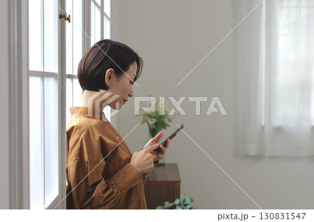 窓辺でスマホを操作する女性 窓辺でスマホを操作する女性 130831547