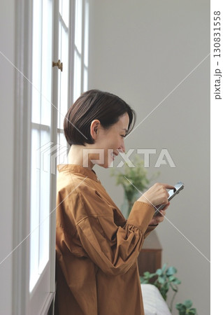 窓辺でスマホを操作する女性 130831558