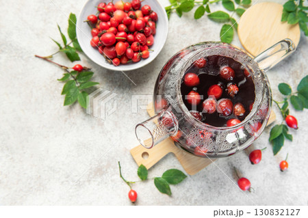 Steaming rosehip tea brewing in glass teapot with fresh rose hips 130832127