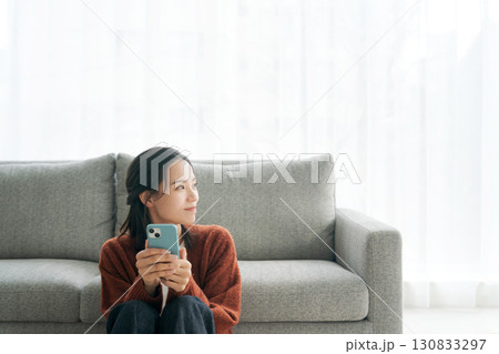 リビングでスマホを操作する若い女性 130833297
