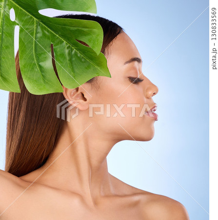 Woman, leaf and natural beauty in organic skincare cosmetics for self love or care against blue studio background. Relaxed female with leafy green plant for sustainable health, eco wellness or facial Woman, leaf and natural beauty in organic skincare cosmetics for self love or care against blue studio background. Relaxed female with leafy green plant for sustainable health, eco wellness or facial 130833569