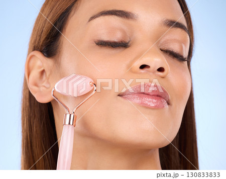 Skincare, massage and woman rolling face, anti aging morning beauty routine on blue background. Cosmetics, skin repair and hispanic model with rose stone quartz facial roller product in studio promo. 130833833