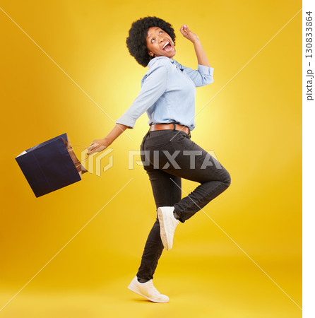 Bag, happy and black woman shopping, excited and celebrating sale in studio on yellow background. Discount, shopper and girl customer cheerful after boutique, retail or store deal posing isolated 130833864
