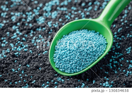 Green scoop with fertilizer blue granules. Granular chemical fertiliser for plant over soil background. Role of nutrients mineral in plants growth, soil life. Space for text. Gardening time. Planting 130834638