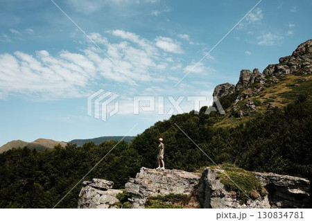 A young woman stands on a cliff in Stara Planina National park, Serbia country, admiring vast green mountains under a blue sky. A perfect moment of freedom and adventure in nature A young woman stands on a cliff in Stara Planina National park, Serbia country, admiring vast green mountains under a blue sky. A perfect moment of freedom and adventure in nature 130834781