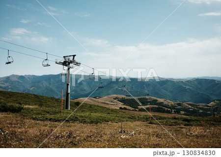 Empty chairlift rising above the green slopes of Stara Planina under a bright summer sky, with panoramic mountain views in the distance. Serbia country Empty chairlift rising above the green slopes of Stara Planina under a bright summer sky, with panoramic mountain views in the distance. Serbia country 130834830