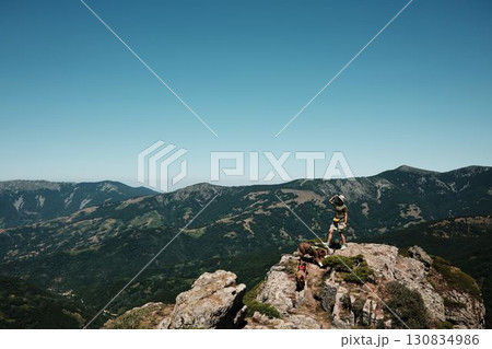 Woman with two dogs German and Australian Shepherd standing on rocky cliffs of Stara Planina, overlooking vast mountain valleys and dramatic landscapes. Travel and hiking with pets concept 130834986