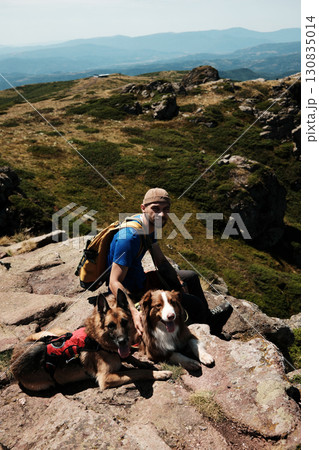 Smiling male hiker with backpack resting on a rock with two dogs German and Australian Shepherd in Stara Planina mountains. Travel and hiking with pets concept Smiling male hiker with backpack resting on a rock with two dogs German and Australian Shepherd in Stara Planina mountains. Travel and hiking with pets concept 130835014