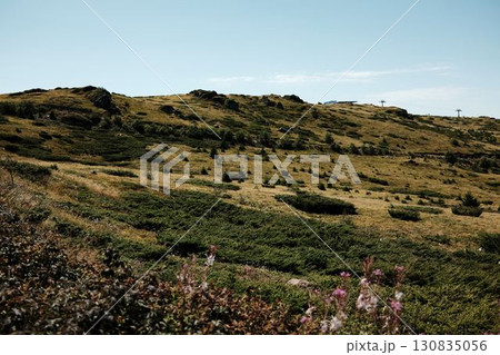 Open grassy plateau of Stara Planina with scattered rocks and distant ski lift under summer sky. Serbia country Open grassy plateau of Stara Planina with scattered rocks and distant ski lift under summer sky. Serbia country 130835056