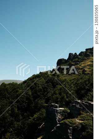 Rugged rocky peaks of Babin Zub mount in Stara Planina rising above lush green hills under bright summer sky. Serbia country Rugged rocky peaks of Babin Zub mount in Stara Planina rising above lush green hills under bright summer sky. Serbia country 130835065