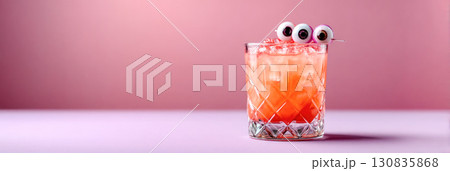 Colorful Halloween cocktail in a glass with playful eyeball garnish, set against a soft pink background, perfect for festive celebrations 130835868