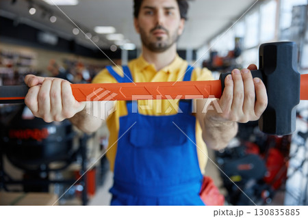A man worker in work clothes holds a large hammer, showcasing skill 130835885