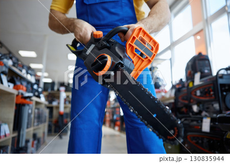 A male worker is holding a chainsaw inside a store 130835944