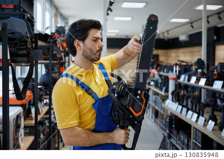 A man worker is holding a chainsaw inside a hardware store 130835948