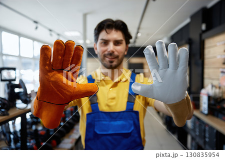 Male young worker holds two pairs of gloves Male young worker holds two pairs of gloves 130835954
