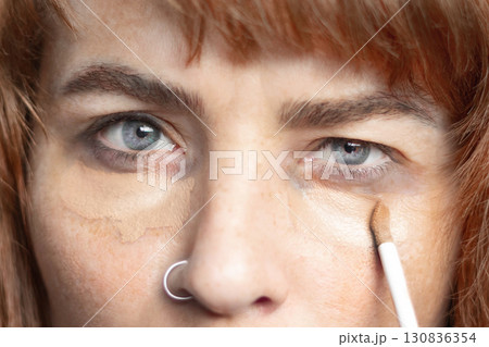 Woman smears dark circles under her eyes with concealer, foundation. Bruises under the eyes, bags under the eyes, dark circles under the eyes. Close up photo Woman smears dark circles under her eyes with concealer, foundation. Bruises under the eyes, bags under the eyes, dark circles under the eyes. Close up photo 130836354