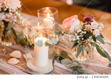 Elegant table decorated with glowing candles and fresh floral arrangements, perfect for creating a romantic atmosphere. Soft candlelight complements the delicate blooms beautifully. Elegant table decorated with glowing candles and fresh floral arrangements, perfect for creating a romantic atmosphere. Soft candlelight complements the delicate blooms beautifully. 130836469