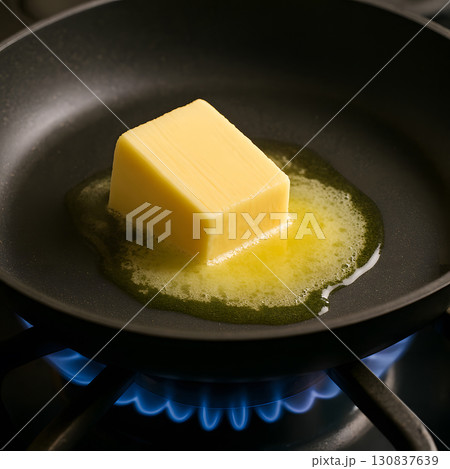 Butter cube melting in frying pan with blue flame below 130837639