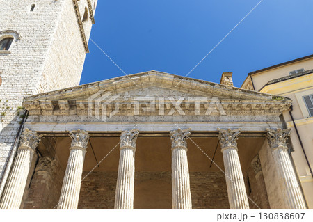 Temple of Minerva in Assisi showcasing corinthian columns and roman architecture against blue sky Temple of Minerva in Assisi showcasing corinthian columns and roman architecture against blue sky 130838607
