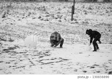 Two individuals sculpt snowballs in a snowy landscape, creating winter fun. Two individuals sculpt snowballs in a snowy landscape, creating winter fun. 130838890