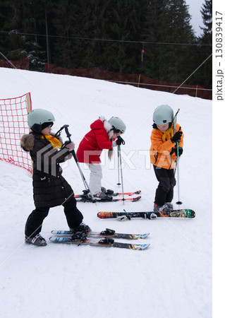 Snowy day adventure with young skiers practicing skills at a local mountain resort surrounded by towering trees and gentle slopes on a crisp winter morning Snowy day adventure with young skiers practicing skills at a local mountain resort surrounded by towering trees and gentle slopes on a crisp winter morning 130839417