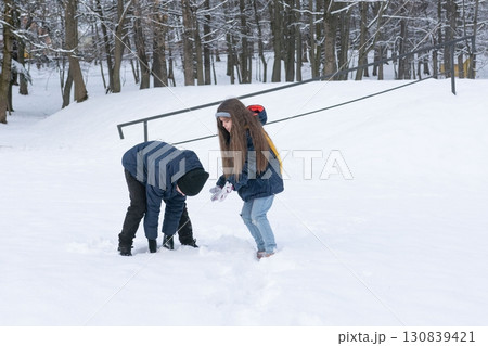Children playfully build a snow fort together in a snowy park, enjoying winter's fun. Children playfully build a snow fort together in a snowy park, enjoying winter's fun. 130839421