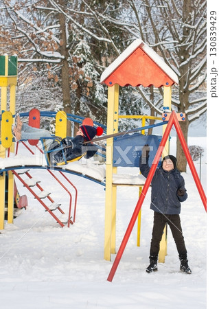 Children playing on a snowy playground. One child swings while another waits. Children playing on a snowy playground. One child swings while another waits. 130839429