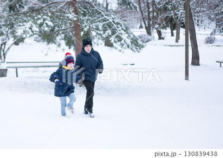 Two children joyfully run through a snow-covered park, their winter attire bright against the white landscape. Two children joyfully run through a snow-covered park, their winter attire bright against the white landscape. 130839438
