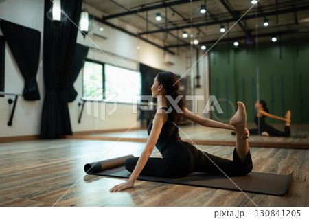Flexible young woman performing pigeon pose variation during yoga training indoors Flexible young woman performing pigeon pose variation during yoga training indoors 130841205
